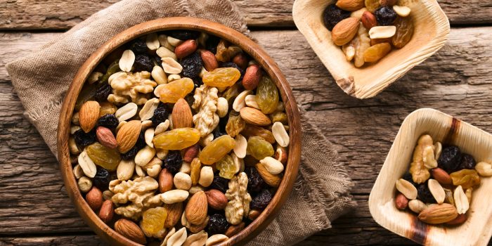 Healthy trail mix snack made of nuts (walnut, almond, peanut) and dried fruits (raisin, sultana) in wooden bowl, photographed overhead (Selective Focus, Focus on the trail mix in the big bowl)